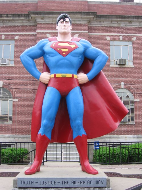 A large Superman statue stands proudly, wearing his iconic blue and red costume, with a cape and a strong pose.