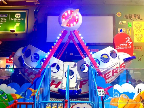 Colorful amusement ride shaped like an airplane, featuring bright lights and a playful design in a family entertainment center.
