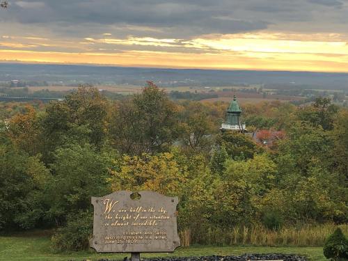 A scenic view of rolling hills and a sunset, featuring a stone monument with an inscription by Elizabeth Ann Seton.
