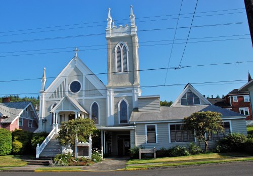 A large, historic church with a tall steeple, surrounded by greenery and residential buildings under a clear blue sky.