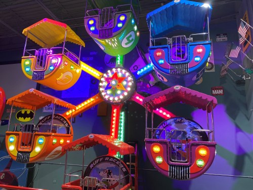 Colorful indoor amusement ride with illuminated cabins, featuring a star design and playful themes like Batman.