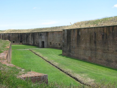 A grassy area surrounded by tall brick walls of a historic fort, with a doorway visible in the distance.
