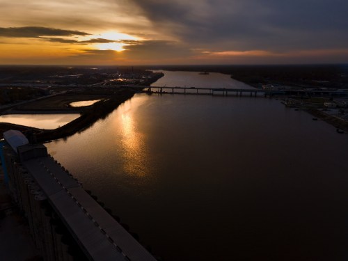 Aerial view of a river at sunset, with a bridge and cityscape reflecting on the water's surface.