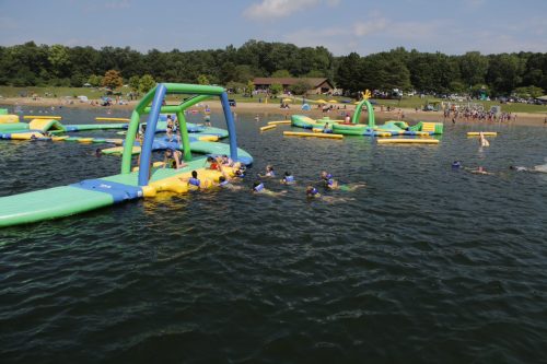 A vibrant water park scene with inflatable structures and people swimming in a lake on a sunny day.