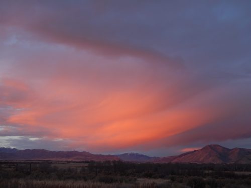 A colorful sunset with pink and purple clouds over a mountainous landscape.