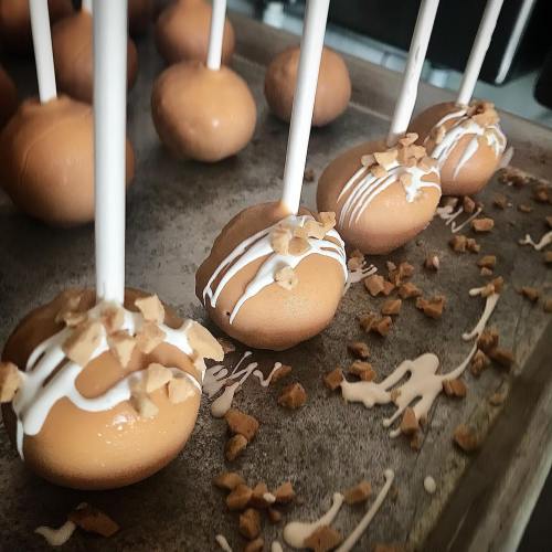 Close-up of cake pops with a caramel coating, drizzled with white icing and topped with crushed toffee bits.