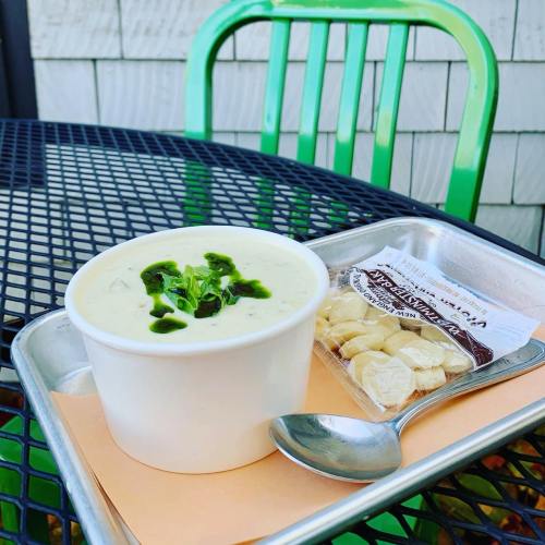 A bowl of creamy soup topped with herbs, served with a spoon and a side of nuts on a metal tray, on a green table.
