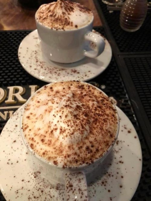 Two cups of cappuccino topped with frothy milk and cocoa powder, served on white saucers.