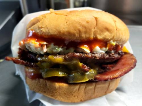 A hearty burger with layers of beef, bacon, cheese, pickles, and sauces, served in a soft bun.