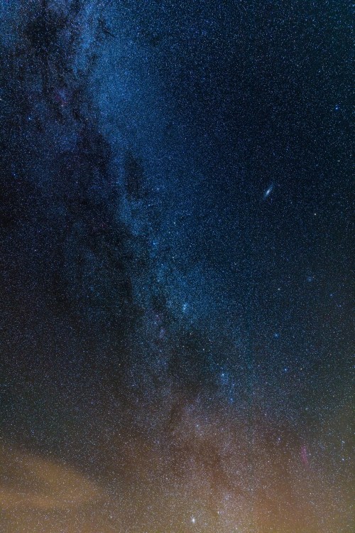 A stunning night sky filled with stars, showcasing the Milky Way and a distant galaxy against a dark backdrop.