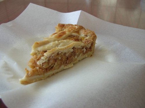 A slice of pastry with a golden-brown crust and a filling of nuts and sweet ingredients on a white paper.