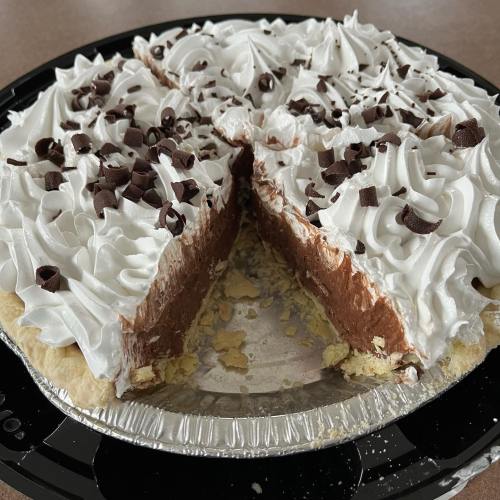 A chocolate cream pie with whipped cream topping and chocolate shavings, partially sliced on a black plate.