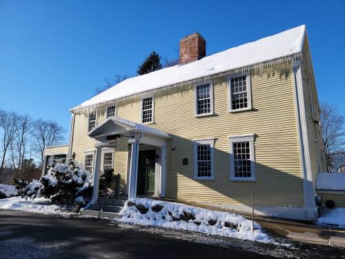 A yellow two-story house with a snow-covered roof, surrounded by snow and clear blue skies.