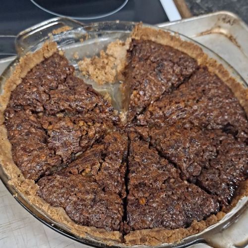 A baked pie with a dark, textured filling and a golden crust, sliced into eight pieces in a glass pie dish.