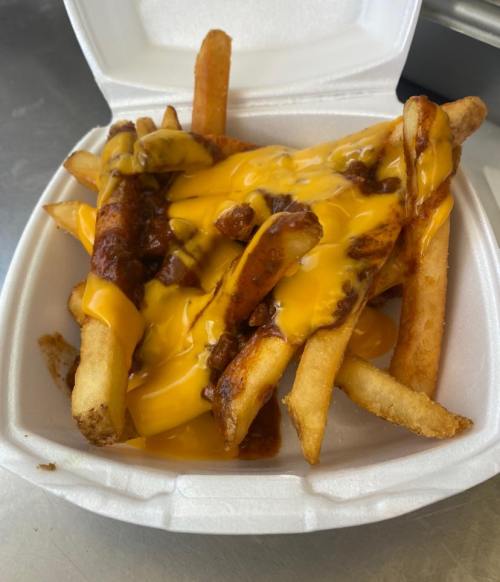 A takeout container filled with French fries topped with melted cheese and chili.