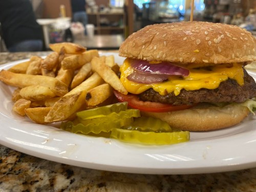 A juicy cheeseburger with lettuce, tomato, onions, and pickles, served with a side of golden French fries.