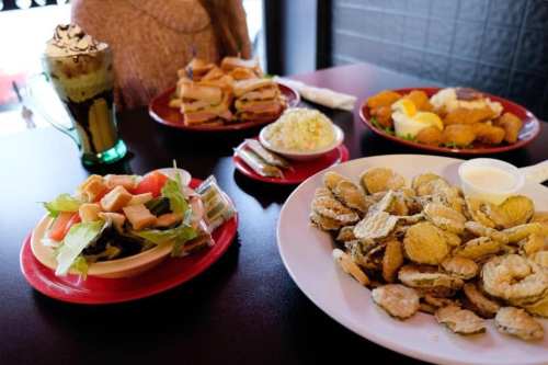 A table spread with fried oysters, a salad, sandwiches, and a dessert drink in a cozy dining setting.
