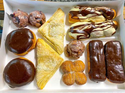 A box of assorted pastries including chocolate-covered donuts, cream-filled pastries, and flaky pastries.