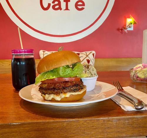 A delicious burger with lettuce and tomato on a plate, alongside a drink in a jar, set against a red café wall.