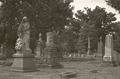 A serene cemetery scene featuring ornate gravestones and statues surrounded by lush trees.
