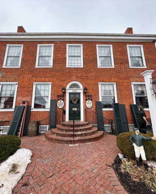 Historic brick building with green door, large windows, and a welcoming entrance, surrounded by snow and greenery.