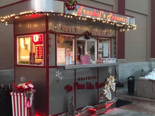 A festive popcorn stand decorated with lights and holiday decor, featuring a sign that reads "No Place Like Home."