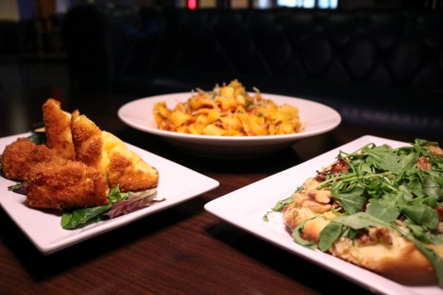 A table with three dishes: crispy fried items, a pasta dish, and a flatbread topped with greens.
