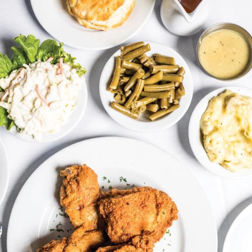 A plate of fried chicken with sides of green beans, coleslaw, mashed potatoes, and a biscuit, plus gravy and sauce.