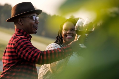 A couple toasting with wine glasses outdoors, smiling and enjoying a sunny moment together.