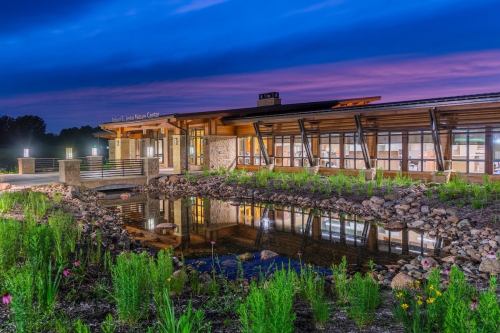 Modern building with large windows beside a pond, surrounded by greenery, under a twilight sky.