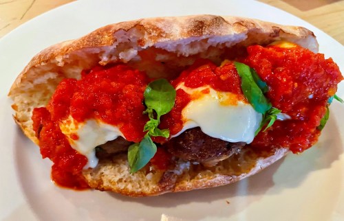 A meatball sandwich with marinara sauce, mozzarella, and fresh basil on a toasted roll.