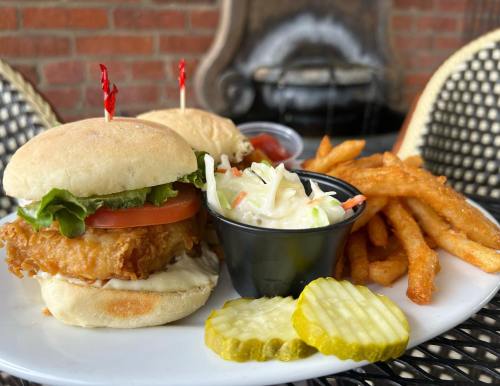 A plate with two chicken sandwiches, coleslaw, fries, and pickles, garnished with red flags on the sandwiches.