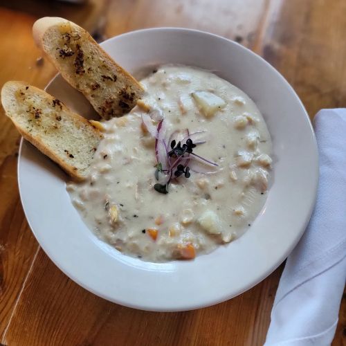 A bowl of creamy seafood chowder garnished with microgreens, served with two slices of toasted garlic bread.