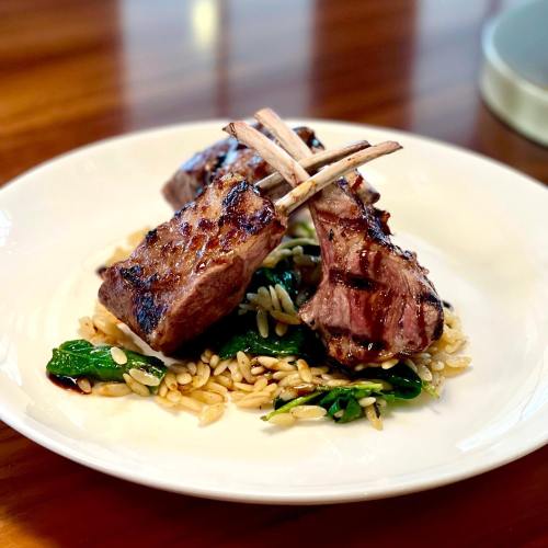 Grilled lamb chops on a bed of orzo and spinach, served on a white plate with a wooden table background.