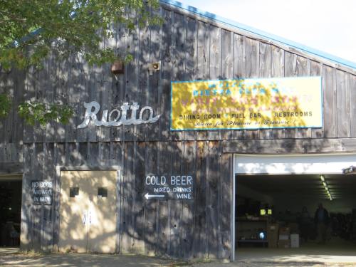 A rustic wooden building with a sign for a dining room, bar, and restrooms, featuring "Cold Beer" on the door.