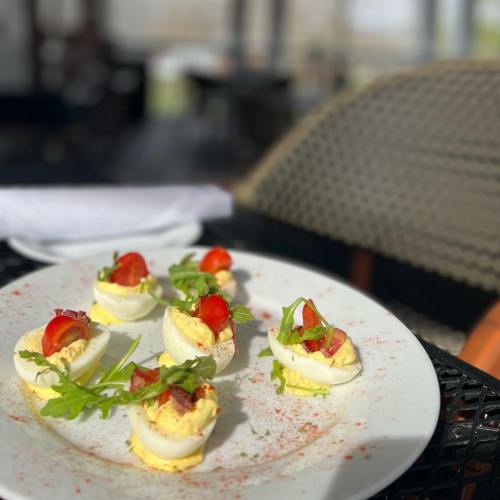 A plate of deviled eggs topped with cherry tomatoes and arugula, sprinkled with paprika, on a table.