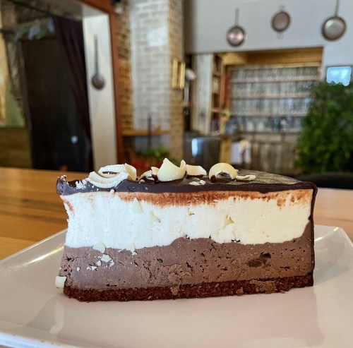 A slice of layered chocolate and cream cake topped with white chocolate shavings, served on a white plate.