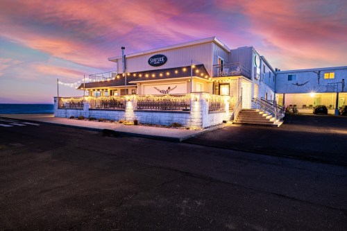 A coastal building at sunset, featuring outdoor lighting and a welcoming entrance, with a view of the ocean.