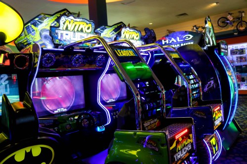 Colorful arcade machines with neon lights, featuring racing games like "Nitro Trucks" and "Halo."