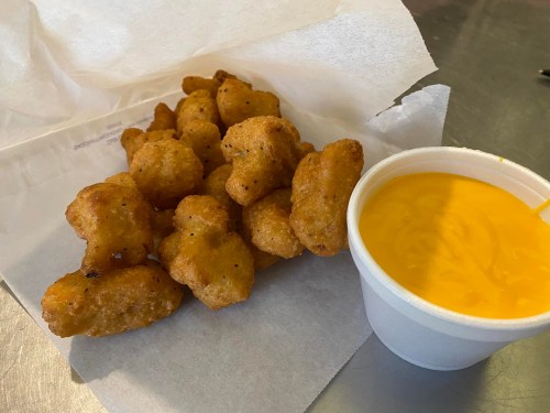 A serving of golden-brown fried snacks next to a cup of creamy cheese sauce on a paper tray.