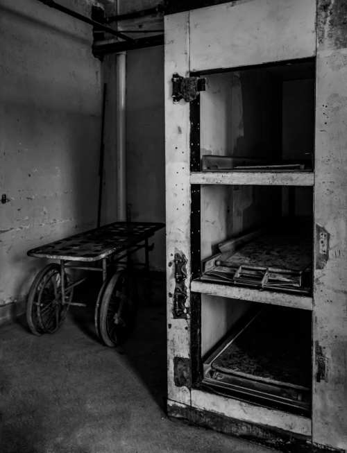 A dimly lit, abandoned room featuring a metal storage unit and a wheeled cart, evoking a somber atmosphere.