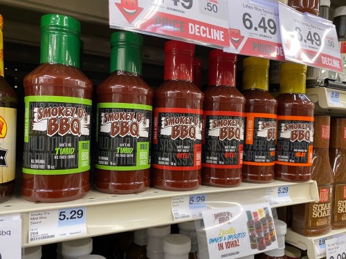 Bottles of Smokey D's BBQ sauce lined up on a store shelf, featuring various flavors and prices.