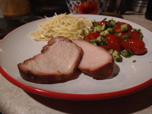 A plate with sliced pork, spaghetti, and a fresh salad of tomatoes and cucumbers.