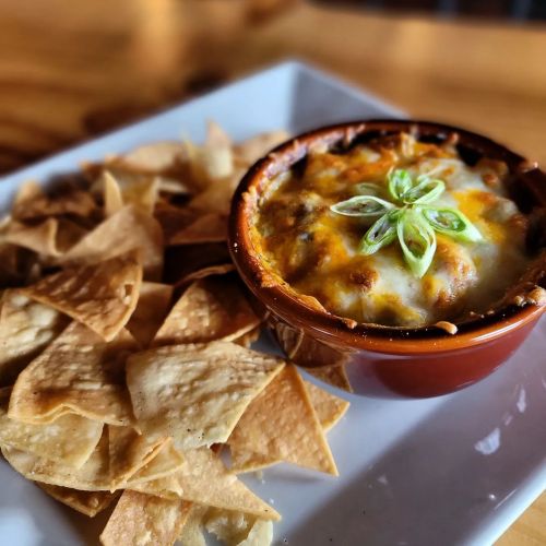 A bowl of cheesy baked dip topped with green onions, served with crispy tortilla chips on a white plate.