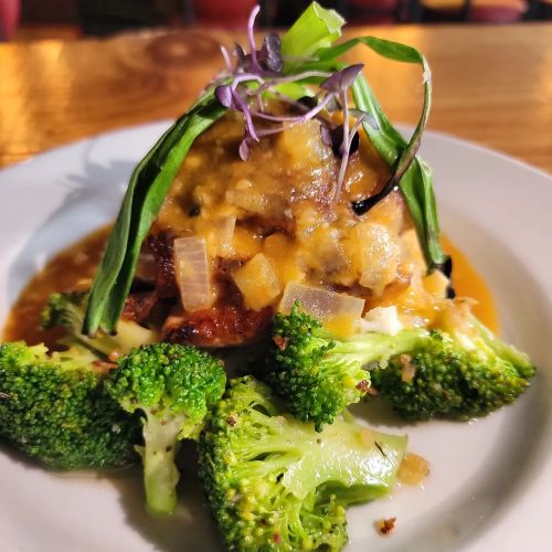 A plate of sautéed broccoli topped with a savory dish featuring diced vegetables and a drizzle of sauce.
