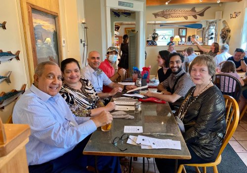 A group of five people sitting at a restaurant table, smiling and enjoying their meal together.