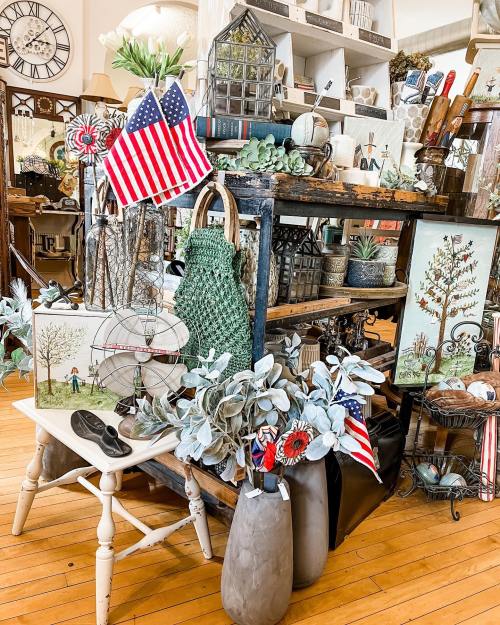 A cozy shop display featuring plants, decor, and small American flags on a wooden table and shelves.