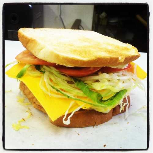 A sandwich with toasted bread, layers of lettuce, tomato, and cheese, sitting on a white surface.