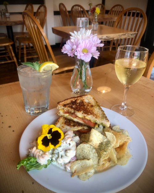 A plate with a grilled cheese sandwich, salad, chips, a glass of water, and a glass of white wine on a wooden table.