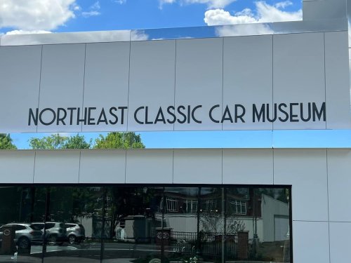 Sign for the Northeast Classic Car Museum, featuring modern architecture and a clear blue sky.